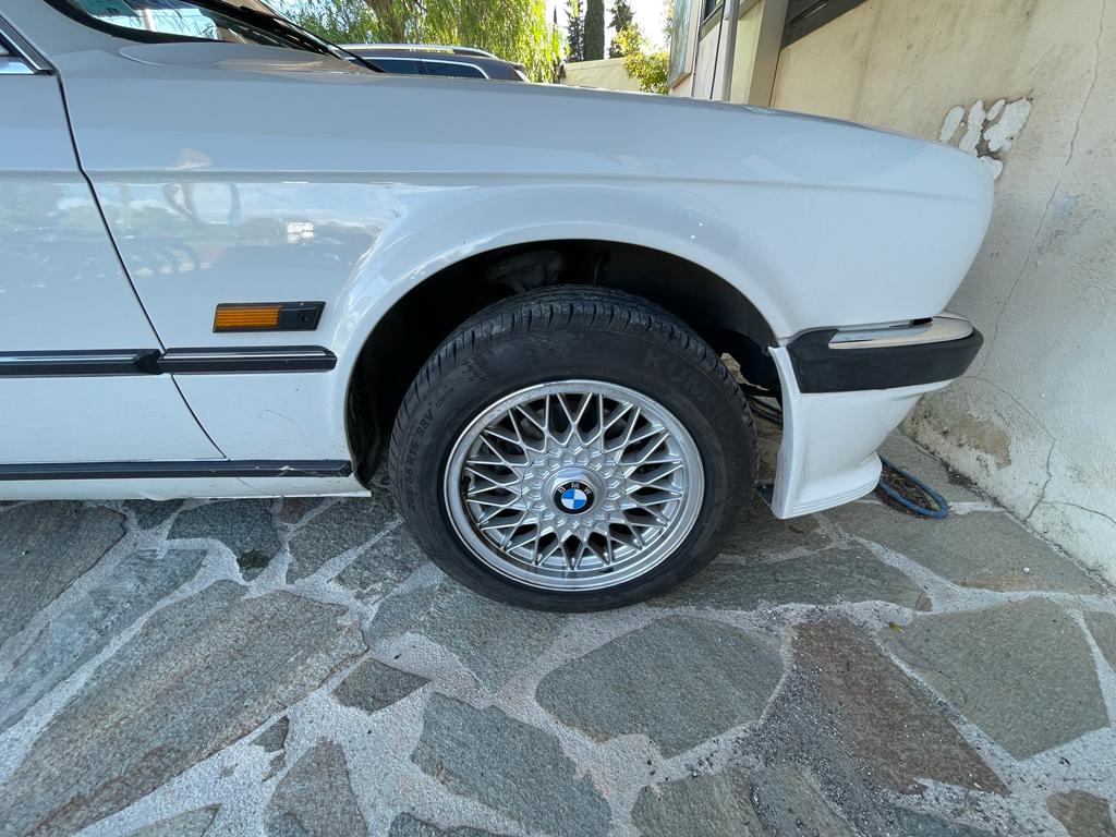 Roue BMW E30 avec jante BBS et cache moyeu BMW bleu blanc installé vue rapprochée quartier avant